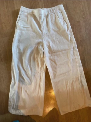 Vita sommarbyxor från Cavalere - Säljer ett par vita byxor från Cavalere med hög midja. Byxorna har sidfickor fram och diskreta fickor bak (som är ihopsydda), samt dragkedja vid höften. Materialet är mjukt och luftigt. Perfekta för dig som gillar stilrena och bekväma byxor. Ett litet hål på ena sidan (se bild)