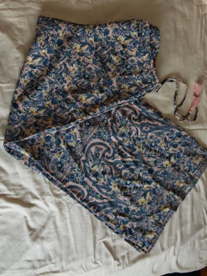 Blommiga vida byxor i istr.46 från indiska - Säljer ett par supermysiga vida byxor från indiska med blommigt mönster i blått, gult och rosa. Byxorna har snörning i midjan med rosa tofsar och är gjorda i mjuk viskos. Inner mått 76 Perfekta för dig som gillar färgglada och unika plagg!
