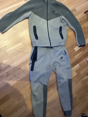Nike tech grön - Nike mjukisbyxor i två nyanser av grått och grönt, med ribbade muddar och svarta dragkedjor på fickorna. Byxorna har en slim passform och är tillverkade i mjukt bomullsmaterial. Snyggt broderad Nike-logga på benet och praktisk snörning i midjan.