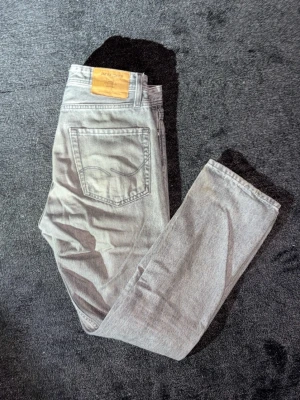 Levi's 501 grå jeans straight fit - Säljer ett par Levi's 501 jeans i grå tvätt med klassisk straight fit. Jeansen har fem fickor, knappgylf och den ikoniska läderpatchen bak i midjan. Materialet är slitstark bomullsdenim och passformen är normal med raka ben.