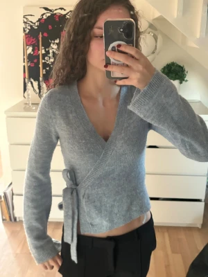 Ljusblå omlottkofta med knyt - Supermysig ljusblå omlottkofta med knyt i sidan och v-ringning. Den är ifrån Gina Tricot i storlek Xs. Koftan är stickad och har långa ärmar med lite lösare passform. Perfekt att slänga på sig när det är lite kyligt ute.