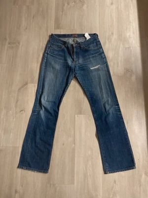 Blå jeans från Big Star - Säljer ett par klassiska blå jeans från Big Star. Jeansen har fem fickor, slitningar på framsidan och snygga detaljer på bakfickorna. Materialet är robust denim och färgen är mörkblå med ljusare tvättade partier. Perfekt för dig som gillar en avslappnad stil.