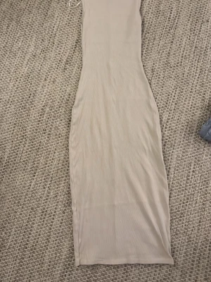 Beige ribbad långklänning - Säljer en enkel och stilren beige långklänning i ribbat material. Klänningen har en kroppsnära passform och är ärmlös.
