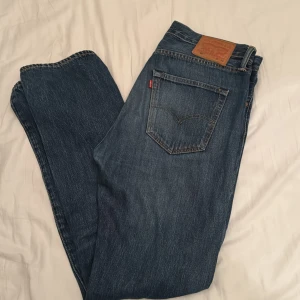 Levi's 501 jeans blå W32 L34 - Klassiska Levi's 501 jeans i mörkblå tvätt med raka ben och fem fickor. Snyggt läderpatch bak i midjan och ikonisk röd Levi's-tagg vid bakfickan. Jeansen är tillverkade i slitstarkt bomullsdenim och har knappgylf framtill.