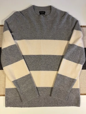 Randig grå och vit tröja Massimo Dutti (cashmere) - Snygg stickad tröja från Massimo Dutti i storlek M, med breda horisontella ränder i grått och vitt. Tröjan har rund hals och ribbade muddar vid ärmslut och nederkant. Tillverkad i mjuk ull och kashmir för extra komfort och stil. Använd bara 2 gånger. Unisex.
