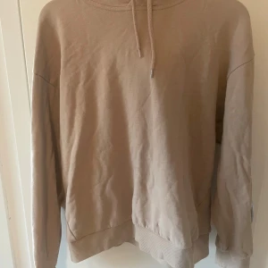 Beige hoodie från 157 med huva - Säljer en beige hoodie från 157 i storlek M. Tröjan har en klassisk huva med snörning och ribbade muddar vid ärmslut och nederkant. Materialet är mjukt och skönt, perfekt för chill dagar. Enkel och stilren design utan mönster eller tryck.