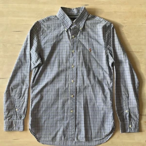 Blårutig skjorta från Ralph Lauren - Snygg blårutig skjorta från Ralph Lauren i slim fit-modell. Skjortan har klassisk krage, knappar hela vägen och det ikoniska broderade Polo-logot på bröstet. Tillverkad i mjuk bomull, perfekt för dig som gillar stilren och tidlös design.