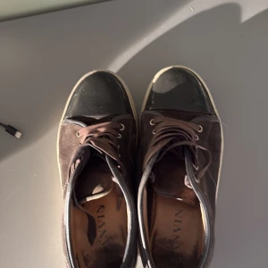 Svarta sneakers från Lanvin med mocka - Snygga svarta sneakers från Lanvin med ovandel i mocka och tåparti i blankt material. Skorna har rund tå, snörning och vita sulor som ger en schysst kontrast. Perfekta för dig som gillar stilrena och exklusiva sneakers med coola detaljer.