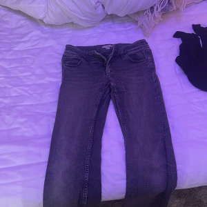 Svarta/ grå butcut jeans med dubbla knappar - Snygga svarta/ grå jeans med utsvängda ben och dubbla silverfärgade knappar i midjan. Klassisk femficksmodell med en ficka som har lock och knapp. Jeansen har normal passform och är tillverkade i slitstarkt jeanstyg.