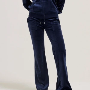 Mörkblå juicy byxor med fickor - Snygga mörkblå mjukisbyxor i mjuk velour med breda ben och coola fickdetaljer både fram och bak. Byxorna har snörning i midjan och silverfärgade knappar på bakfickorna. Perfekta för en chill och trendig look.