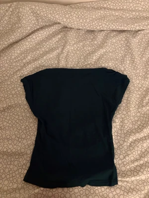 Mörkgrön enkel topp med kort ärm - Säljer en stilren mörkgrön topp med korta ärmar och rak passform. Toppen har en minimalistisk design utan mönster eller detaljer, perfekt för dig som gillar en clean look. Materialet känns mjukt och lätt mot huden.