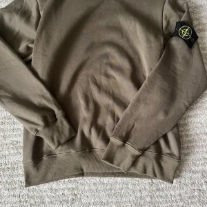 Beige sweatshirt från Stone Island - Säljer en beige sweatshirt från Stone Island med klassisk logotyp-patch på vänster ärm. Tröjan har rund hals, ribbade muddar och är långärmad. Materialet är mjuk bomull som känns skön mot huden. Perfekt för dig som gillar streetwear och snygga detaljer.