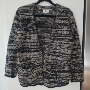 Svartvit stickad kofta från Noa Noa i ull och alpacka  - Mysig stickad kofta från Noa Noa i svart och vitt med coolt mönster. Koftan har två fickor framtill, lång ärm och öppen front. Perfekt för lager-på-lager och chill höst- eller vinterstil. Ull och alpacka gör den mjuk och varm i vinter.