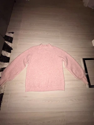Ljusrosa stickad tröja KappAhl S - Mysig ljusrosa stickad tröja från KappAhl i storlek S. Tröjan har en högre hals, ribbade muddar och långärmade ärmar med lite puff. Materialet är mjukt och ger en chill vibe, perfekt för kalla dagar. Enkel och snygg att matcha med jeans eller kjol.