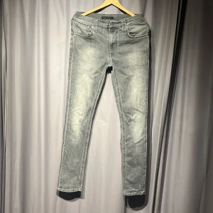 Grå jeans från Nudie Jeans Co - Snygga grå jeans från Nudie Jeans Co med klassisk femficksdesign och svarta läderpatch bak. Jeansen har en rak passform och subtila slitningar framtill för en cool look. Nypris 1699kr