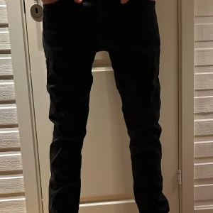 Jack & Jones jeans - Säljer ett par svarta manchesterbyxor med smal passform och klassisk rak design. Byxorna har fickor både fram och bak, och är perfekta för dig som gillar en stilren look med lite edge. Materialet är mjukt och ger en snygg textur till outfiten. Storlek 32/34, slim Glenn 