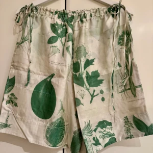 Oversized shorts från Tiger of Sweden - Unika shorts från Tiger of Sweden Spring/Summer 2020 med grönt botaniskt mönster på vit bakgrund. Modellen har hög midja med snörning i sidorna och två fickor bak. 