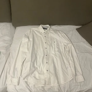 Vit skjorta från Dressmann, storlek M - Klassisk vit skjorta från Dressmann med button-down krage och bröstficka. Skjortan har långa ärmar med manschettknappar och är tillverkad i mjuk bomull. Perfekt för dig som gillar stilrena och enkla plagg med snygga detaljer som knappar och diskret sömnad.