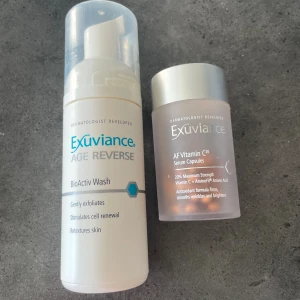 Exuviance BioActiv Wash & Vitamin C20 - Två hudvårdsprodukter från Exuviance: BioActiv Wash i vit plastflaska med pump, som exfolierar och stimulerar cellförnyelse, samt AF Vitamin C20 Serum Capsules i frostad burk med silverlock, med kapslar som innehåller C-vitamin och aminosyror för att ge lyster och jämnare hud.