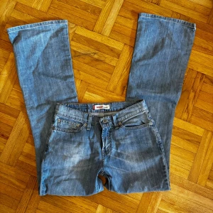 Blå jeansbyxor från Levi's - Ett par blå jeansbyxor från Levi's i en klassisk design. Byxorna har en rak passform och är tillverkade i jeansmaterial. De har en låg midja och är i välanvänt skick.