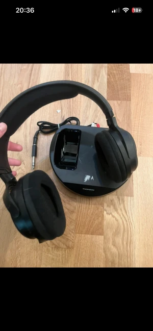 Thomson WHP3001BK trådlösa hörlurar - Bekväma trådlösa over-ear hörlurar med laddningsstation. Modell WHP3001BK. Komplett med kabel och basstation. Mindre kosmetiskt slitage på basstationen, annars i gott skick. Perfekt för TV eller musik utan sladdar. Detta var en present därav utan förpackning vet tyvärr inte hur de fungerar