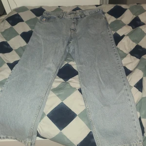 Wide ljusblå jeans från 93Denim - Säljer ett par ljusblå jeans från 93Denim med bred passform och cool broderad figur på fickan. Jeansen har klassisk femficksdesign, gul kontrastsöm och är tillverkade i slitstarkt denimtyg. Perfekt för dig som gillar streetwear och unik stil. Storlek M