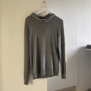 Grå hoodie i kashmir från Oscar Jacobson - Grå Kashmir hoodie från Oscar Jacobson. Tröjan är stickad i kashmir och har en huva samt långa ärmar. Perfekt för dig som gillar stilren och enkel design med premiumkänsla. Perfekt nu inför hösten och vintern när det är lite kyligare. Nypris: 1700