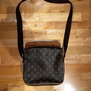  axelväska monogram brun - Snygg axelväska  monogrammönster. Väskan är brun med detaljer i beige och guld, har justerbar axelrem i textil och läderdetaljer. 