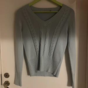 Ljusblå stickad tröja More & More - Supersnygg ljusblå stickad tröja från More & More med v-ringad hals och flätade detaljer framtill. Tröjan har långa ärmar och bred ribbad kant vid midja och ärmslut. Perfekt för dig som gillar stilrena och mjuka plagg med lite extra twist.