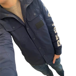 Replay jacka - Snygg marinblå vindjacka från Replay i mycket bra skick med stor vit logga längs ena ärmen. Jackan har huva, knappar framtill och praktiska fickor på bröstet. 