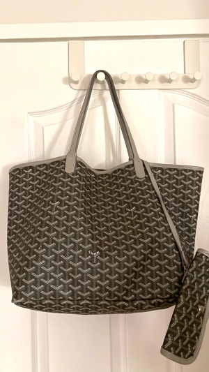 G- yard väska med mönster - Snygg shoppingväska i grått och vitt med ikoniskt grafiskt mönster. Väskan har långa handtag och matchande liten clutch som kan fästas inuti. Tillverkad i slitstarkt syntetmaterial med skinn-detaljer och silverfärgad knapp på clutchen. Skriv för mer info