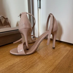 Beige klackpumps från Call It Spring - Snygga beige klackpumps med öppen tå och smal rem runt ankeln från Call It Spring. Skorna har hög klack och en glansig finish i syntetmaterial. Perfekt för dig som gillar stilrena och eleganta skor med en modern touch.