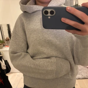 Zara grå hoodie - Säljer en ljusgrå croppad hoodie med huva och magficka. Tröjan har långa ärmar med ribbade muddar och är gjord i mjuk bomullsmix.