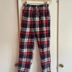 Rutig mjukisbyxa med snörning - Säljer ett par sköna mjukisbyxor med röd, vit och mörkblå rutig design. Byxorna har elastisk midja med snörning och är gjorda i mjukt bomullsmaterial. Perfekta för chill dagar hemma eller när du vill vara extra bekväm.