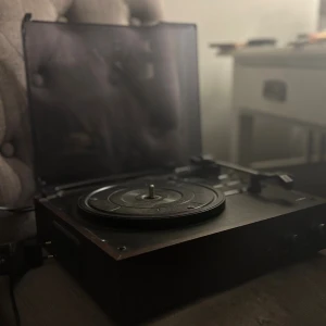 Nedis TURNT200BK Skivspelare - Modern skivspelare från Nedis med tonkontroll, volymratt och hörlursutgång. Utrustad med dammskydd och RCA-utgångar. Skicket är gott med mindre ytslitage på locket. Perfekt för vinylälskare som vill ha både klassisk och modern funktionalitet.