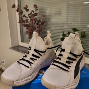 Vita sneakers från Puma strl 42 - Snygga vita sneakers från Puma med svarta detaljer och svart logga på sidan. Skorna har en sportig design med meshpaneler för extra andningsförmåga, svart snörning och robust sula. Perfekta för dig som gillar en clean och modern look.