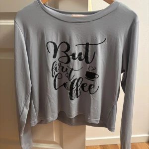 Grå långärmad tröja med tryck - Snygg grå pyjamas långärmad tröja med svart tryck på framsidan där det står 'But first coffee' och en liten kaffekopp. Tröjan har en rund halsringning och är gjord i mjukt bomullsmaterial, perfekt för chill dagar och kaffeälskare. (En till produkt läggs till vid köp:) det blir en överraskning)