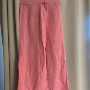 Rosa linnebyxor  - Snygga ljusrosa linnebyxor Byxorna är tillverkade i en skön blandning av linne och viskos, vilket gör dem luftiga och perfekta för varmare dagar. De har en enkel design utan synliga fickor eller detaljer. 