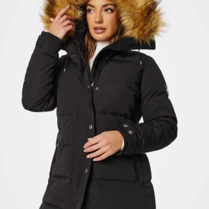 Svart dunjacka med päls på huvan - Säljer en svart dunjacka med fluffig päls på huvan och snygga detaljer som dragkedja och knappar. Jackan är lång och har en schysst passform, perfekt för kalla dagar. Flera fickor med dragkedja och justerbar huva gör den både praktisk och stilren. Kan komma överens med pris!