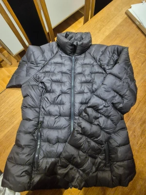 Svart dunjacka från McKinley, strl 36 - Svart tunn dunjacka från McKinley i storlek 36. Jackan har quiltad design, hög krage och två sidofickor med dragkedja. Perfekt för lite kallare dagar med sin lätta och fluffiga känsla. Stängs med dragkedja framtill och har långärmade ärmar.