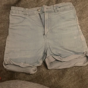 Ljusblå denimshorts med uppvik - Säljer ett par ljusblå denimshorts från Sdenim i storlek 152. Shortsen har klassisk femficksdesign, uppvikta benslut och stängs med dragkedja och knapp. Perfekta för varma dagar och ger en avslappnad vibe.