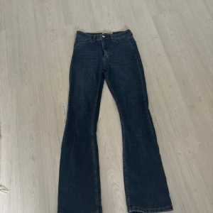 Blå bootcut jeans från Taruk Ekin - Snygga blå jeans från Taruk Ekin i bootcut-modell med klassisk femficksdesign och hög midja. Jeansen har en mörk tvätt och är tillverkade i slitstarkt denimtyg med bälteshällor och knappstängning framtill.