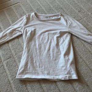 Vit långärmad tröja från 157 - En basic vit långärmad tröja från 157 med rund halsringning. Tillverkad i mjuk bomull, perfekt för lager-på-lager eller som enkel topp. Snygg och enkel modell som passar till allt.