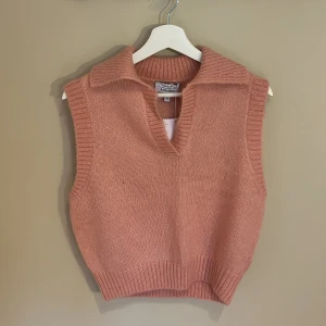 Stickad rosa väst från & Other Stories - Snygg stickad väst i mjuk rosa ton från & Other Stories Paris Atelier. Modellen har bred krage, v-ringning och ribbade kanter. Perfekt att styla över en skjorta för en trendig look perfekt nu för hösten. Materialet är stickat (och obs. skjortan ingår inte). Helt oanvänd med prislappen kvar, orginalpris 690kr🩷🩷