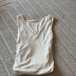 Vit v-ringad ärmlös topp - Säljer en stilren vit ärmlös topp med v-ringning framtill. Toppen har en enkel och clean design som passar perfekt till jeans eller kjol. Materialet känns mjukt och lätt, vilket gör den skön att bära under varma dagar.