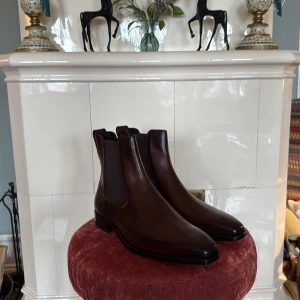 Berluti Chelsea Boots - Säljer ett par Chelsea Boots från Berluti Paris. Bästa läder skorna som finns på marknaden i alla pris klasser. Pris från butik är 25000kr. Allt OG ingår dem är helt nya.          The “plunging” shape of the shoe is reminiscent of the iconic slopes of the “Faraglioni”, the rock formations that rise spectacularly from the sea at Capri. A slender, responsive profile, and a subtle asymmetrical tip transform the model. Crafted from a single piece of arched leather, it moulds perfectly to the instep.
