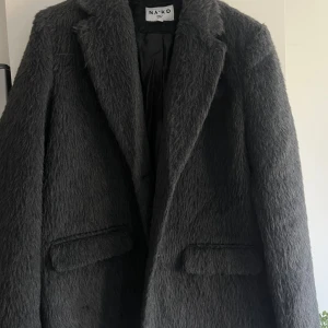 Grå pälskavaj från NA-KD - Säljer en snygg grå pälskavaj från NA-KD med lång luddig struktur och klassisk krage. Jackan har två fickor framtill och är helfodrad för extra komfort. Perfekt för dig som vill ha en statementjacka med cool vibe. I nyskick. 