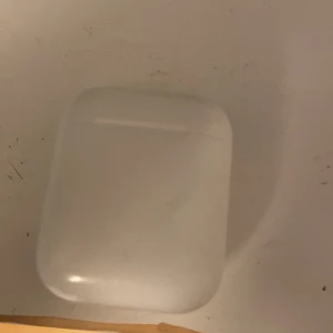AirPods 2 - Apple AirPods 2 med laddningsetui. Trådlösa hörlurar med enkel anslutning till iPhone och andra Apple-enheter. Skicket är begagnat med synliga smutsfläckar och mindre repor på etuiet, men hörlurarna ser hela ut. Perfekt för musik, samtal och träning. Kan absolut rengöras om så önskas!