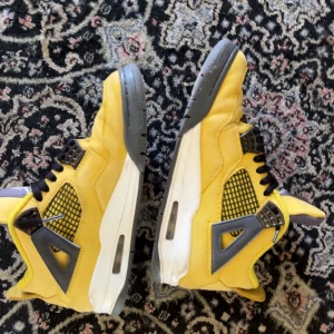 Nike Air Jordan 4 Retro gul/grå - Nike Air Jordan 4 Retro sneakers i en fet gul färg med grå och svarta detaljer. Skorna har meshpaneler på sidorna, synlig Air-sula och klassisk snörning. Materialet är skinn och syntet, med en platt sula och rund tå. Perfekt för dig som vill sticka ut med din sneakerstil.