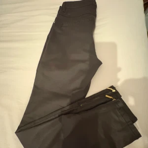 Svarta byxor med dragkedjor från Stockh LM - Snygga svarta byxor från Stockh LM i storlek 38. Byxorna har smal passform och coola guldfärgade dragkedjor vid bensluten. Tillverkade i ett stretchigt material som sitter tajt och bekvämt. Perfekta för dig som gillar en stilren look med en twist.